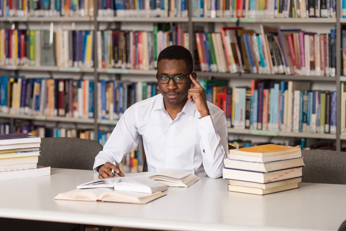 Portrait Of African Clever Student With Open Book Reading It In College Library - Shallow Depth Of Field